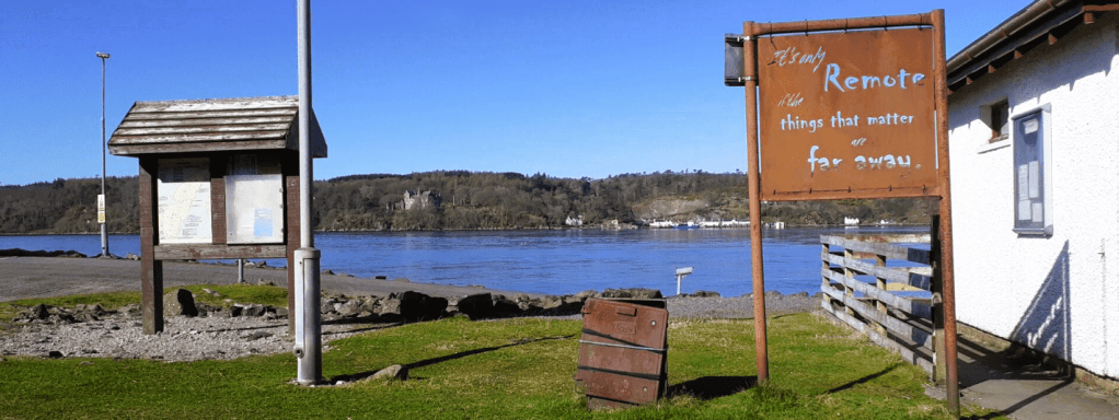 Photo of a rusty signpost next to a building by the sea. The sign reads "It's only remote if the things that matter are far away".